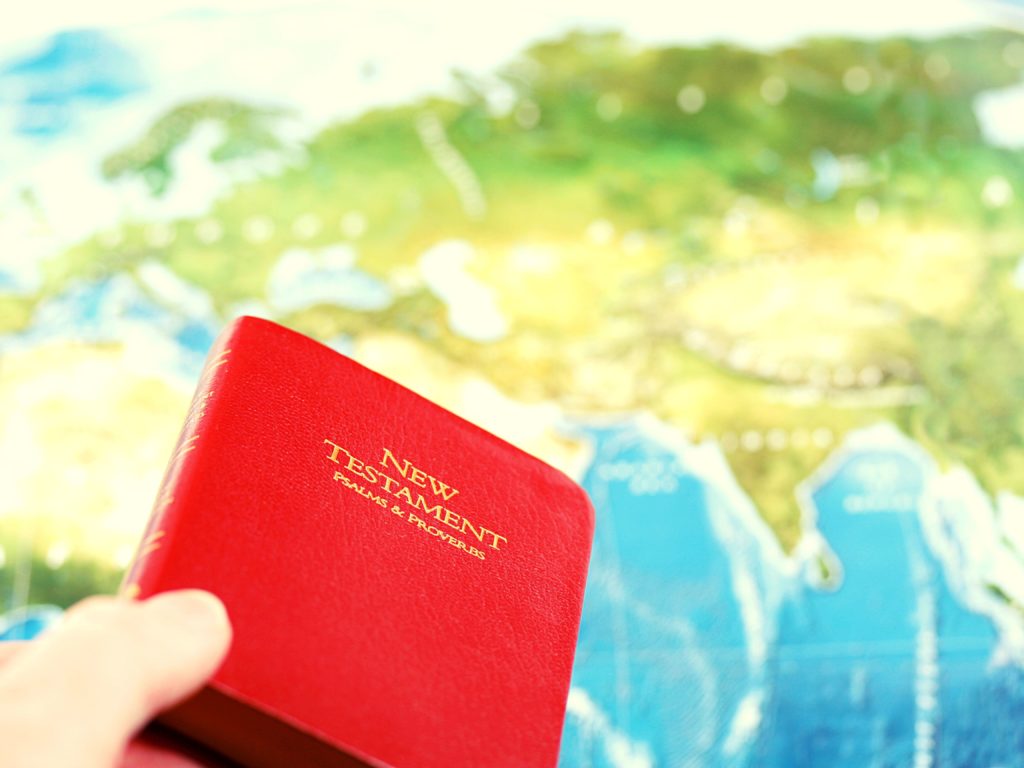 world map and hand holding New Testament | what is a missionary